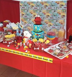 a red table topped with lots of toys and cake next to a wall covered in cartoon characters