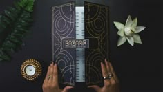 two hands holding a book on top of a table next to a candle and flowers