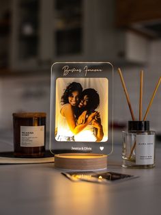 an illuminated photo frame sitting on top of a table next to candles and a candle holder