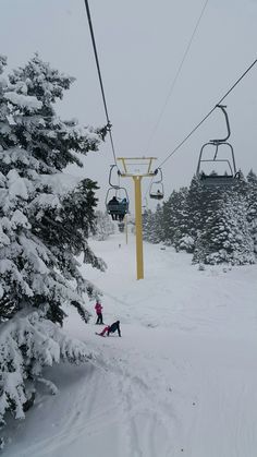 two people skiing down a snow covered slope under a ski lift with trees in the foreground