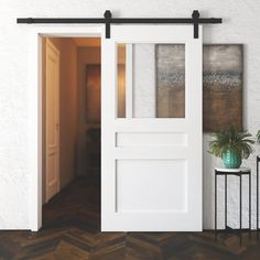 an open white door in a room with wood flooring and potted plant next to it