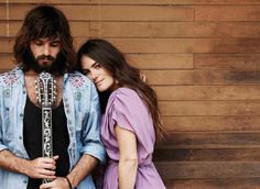 a man and woman standing next to each other in front of a wooden wall with a guitar