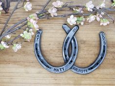 two metal horseshoes sitting on top of a wooden table next to branches with flowers