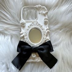 a cell phone with a black bow on it's front and back cover, sitting on a white fur surface