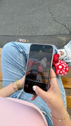 a person sitting on a bench holding a cell phone with minnie mouse stickers on it