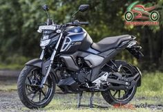 a black motorcycle parked on top of a grass covered field in front of some trees