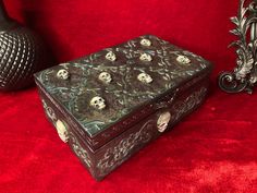 a decorative box with skulls on it sitting next to a black vase and red velvet