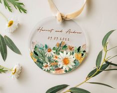 a personalized ornament with flowers and leaves on the front, hanging from a ribbon