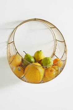 a wire basket filled with fruit on top of a white wall