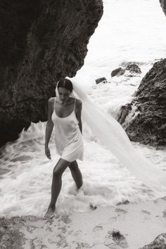 black and white photograph of a man standing in the ocean with his wedding dress flowing over him