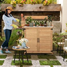 a woman in a hat is watering plants on a small wooden table with two chairs