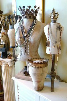 an assortment of necklaces and jewelry on display in front of a mirror, with mannequins