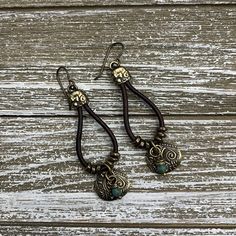 pair of earrings on wooden table with white wood planks in the foreground and dark brown leather cord hanging from them