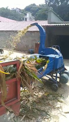 a blue machine that is sitting in the dirt next to some grass and hay on top of it