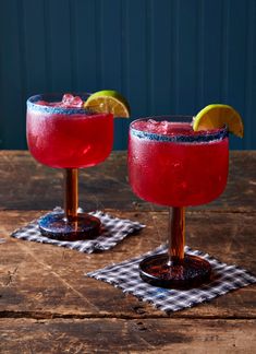 two glasses filled with red drinks sitting on top of a wooden table next to each other