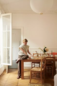 a woman sitting on top of a wooden table in front of a window next to a chair