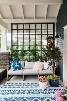 an outdoor living area with blue and white rugs, potted plants and a couch