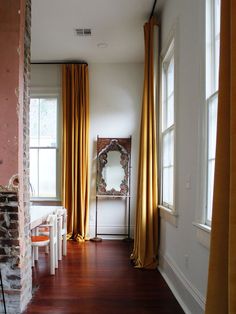 a living room filled with furniture and windows covered in yellow draping next to a brick wall