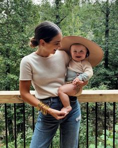 a woman holding a baby in her arms and wearing a large hat on top of her head