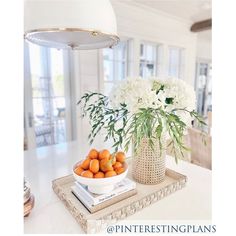 a bowl of oranges sitting on top of a tray next to a vase with white flowers