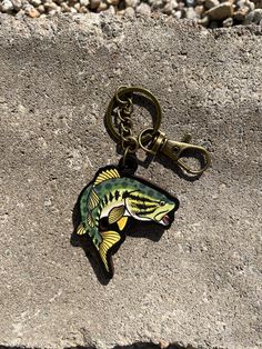 a fish shaped keychain sitting on top of a stone wall next to gravel