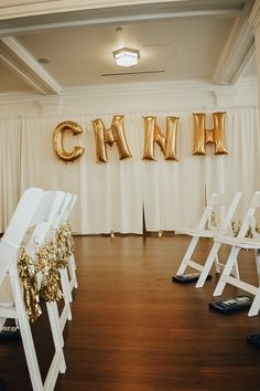 white folding chairs with gold foiled letters and decorations in front of the stage at a wedding