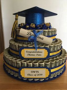 a graduation cake made out of dollar bills and diplomas with blue ribbon on top