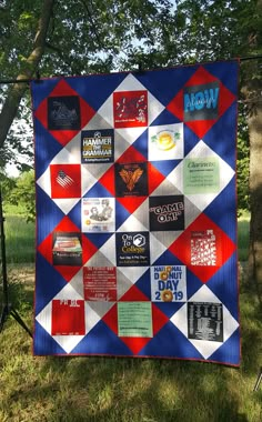 a quilt is hanging on a fence in the grass with trees and bushes behind it