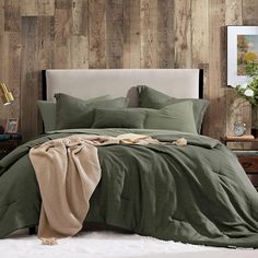 a bed with green sheets and pillows in front of a wood paneled headboard