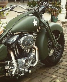 a green motorcycle parked on top of a brick road next to potted planters