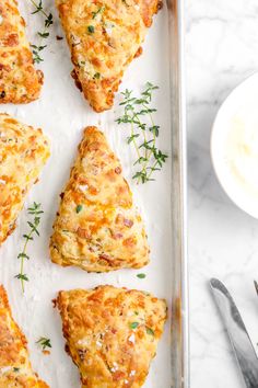 six cheesy scones on a baking sheet next to a bowl of dip