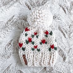 a white knitted hat with red and green flowers on it sitting on a blanket