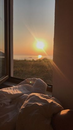 the sun is setting in front of an open window with white sheets and blankets on it