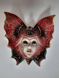 a butterfly shaped mask hanging on the wall next to a white wall with green and red designs