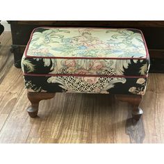 an upholstered foot stool with floral fabric on it, sitting in front of a piano