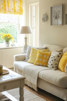 a white couch with yellow and gray pillows in front of a window filled with sunflowers