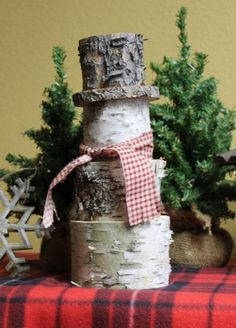 a snowman made out of birch logs sitting on top of a red and white checkered table cloth