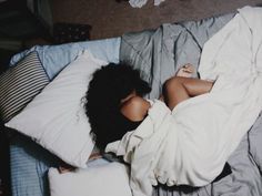 a woman laying on top of a bed covered in white sheets and pillows with her head under the covers