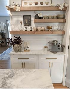 a kitchen with white cabinets and marble counter tops, gold accents on the shelves above