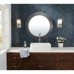 a bathroom vanity with a round mirror above it and wooden drawers underneath the sink, in front of a blue tiled wall