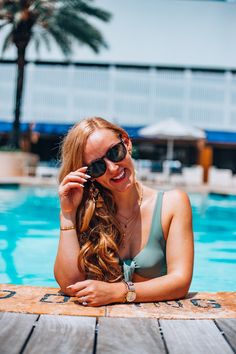 a woman sitting on the edge of a swimming pool with her hair blowing in the wind