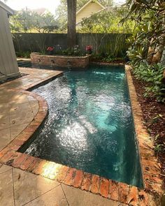 an outdoor swimming pool surrounded by trees and plants in a backyard area with brick edging