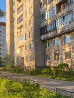 an apartment building with trees and bushes in the foreground, on a sunny day