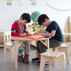 two young boys sitting at a table writing