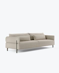 a white couch with four pillows on it's back and arm rests against the wall