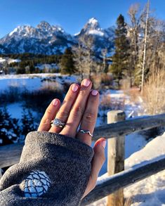 a woman's hand with a ring on it in front of snow covered mountains