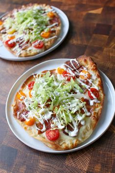 two small pizzas sitting on top of white plates covered in cheese and veggies