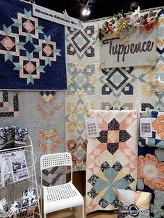 an assortment of quilts on display in a room with white chairs and wall hangings