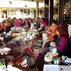 a group of women sitting at tables with cups and plates on them in front of a store