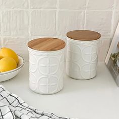 two white canisters sitting on top of a counter next to a bowl of lemons